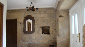 Un pasillo de paredes de piedra con una puerta de madera, un espejo y un cubo de basura.