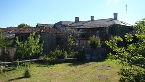 Una casa de piedra tradicional con techo de tejas, rodeada de un jardín cubierto de césped y árboles.