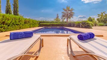 Zona de piscina con sillas de descanso y toallas, rodeada de vegetación y un cielo despejado.