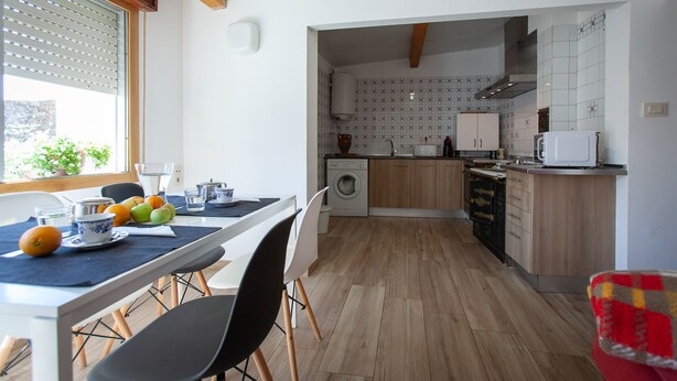 Una cuina moderna amb armaris de fusta, forn integrat i zona de menjador amb taula per a dues persones.