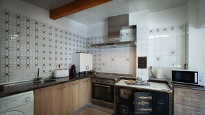 Una cuina amb reixat de rajoles blanques, armaris de fusta, forn de sobre i microones.
