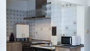 Cuina moderna amb armaris blancs, microones i fogó. Hi ha una taula de dinar amb gots i fruita.