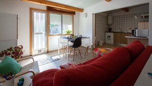 Un saló acollidor amb un sofà vermell, una zona de menjador amb taula i cadires, i una cuina amb rentadora.