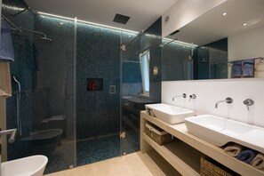 Ein modernes Badezimmer mit einer gläsernen Duschkabine, zwei Waschbecken und einem großen Spiegel.