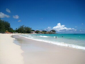 A beach with clear turquoise water, a sandy shore, and a few buildings in the background. - Charming Cottage in Rockley, Barbados only 5 mins Walk to Gorgeous Accra Beach!  (Rockley)