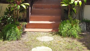 A covered porch with a set of steps leading to a door, surrounded by various plants.