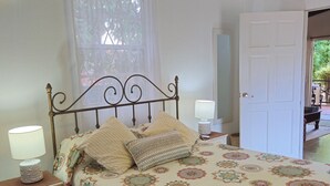 A bedroom with a bed, bedside lamps, a nightstand, a door, and a window with curtains.