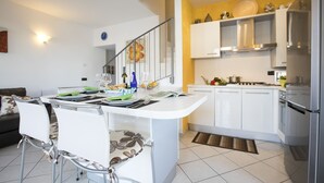 A modern kitchen with white cabinets, a stainless steel refrigerator, and a dining area with a white table and chairs.