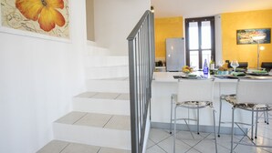 A modern kitchen with a central island, bar stools, and a staircase with a metal railing.