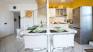 A modern kitchen with a dining area, featuring a stainless steel refrigerator, white cabinets, and a staircase leading to an upper level.