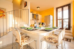 A dining area with a white table set for four, chairs with floral patterns, a kitchen in the background, and a staircase leading to an upper floor. - Blevio Panoramica, Blevio, Italy (Blevio)
