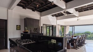 A modern kitchen with a black island, dark cabinetry, and a view of the ocean through large windows.