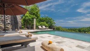 A poolside area with lounge chairs, a stone staircase, and a view of the ocean.