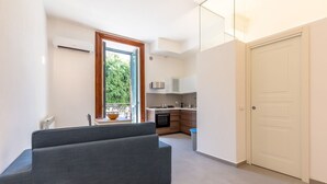 A modern apartment with a grey sofa, a kitchen with white cabinets, and a large window with a view of greenery. - Domus Sicily - Loft Piazza Marina - Palermo (Palermo)