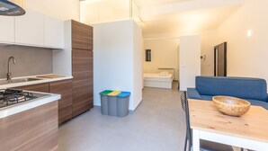 A modern kitchen with a gas stove, wooden cabinets, and a dining area with a blue sofa and a wooden table. - Domus Sicily - Loft Piazza Marina - Palermo (Palermo)