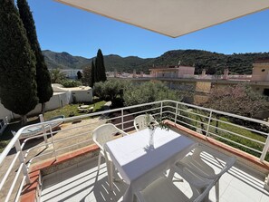 A balcony with a table and chairs, overlooking a mountainous landscape with buildings in the background.