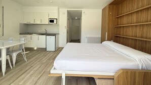 Een kleine kamer met een bed, een kitchenette en een eethoek.