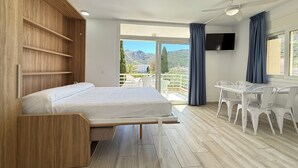 Een slaapkamer met een bed, een houten kledingkast, een balkon met stoelen en een televisie.