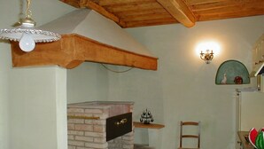 A kitchen with a brick oven, wooden beams, a chair, and a wall-mounted light fixture.