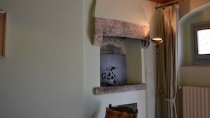 A stone fireplace with a metal sculpture, a wooden ceiling beam, and a window with curtains.