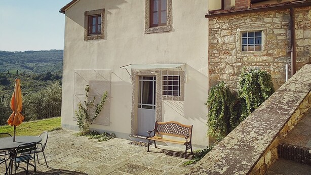A two-story house with a stone facade, a wooden bench outside, and a table with chairs.