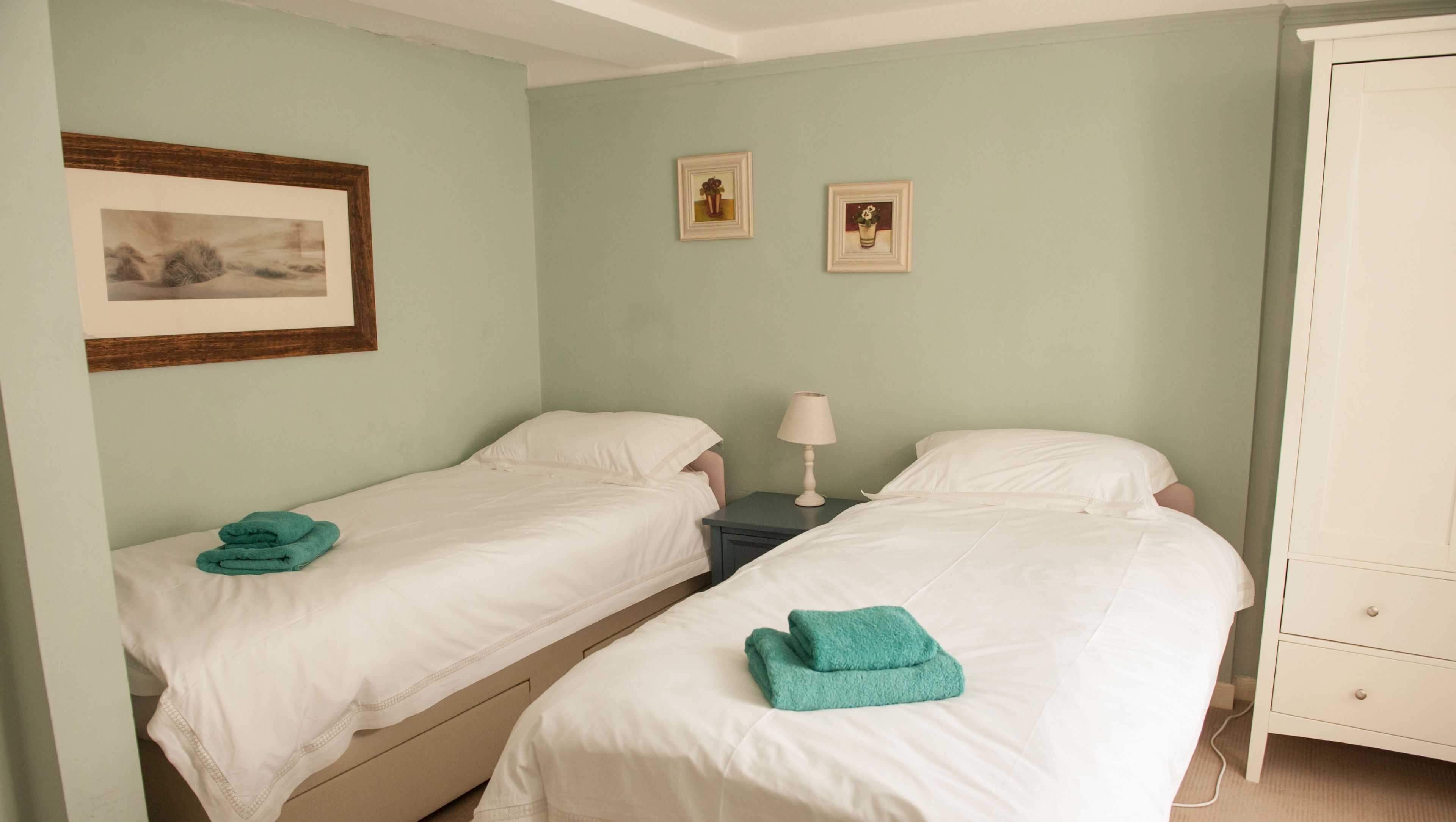A room with two single beds, a nightstand with a lamp, and a cabinet.