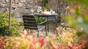 An outdoor dining area with a stone wall backdrop, metal chairs, a table set with a coffee pot, glasses, and a croissant. - Lavender Cottage - sleeps 4 guests  in 2 bedrooms (Lyme Regis)