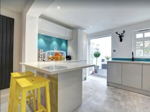 A modern kitchen with a central island, bar stools, a fruit display, and a decorative antler on the wall. - Fully equipped city centre modern townhouse - 5 star rating. (Brighton)