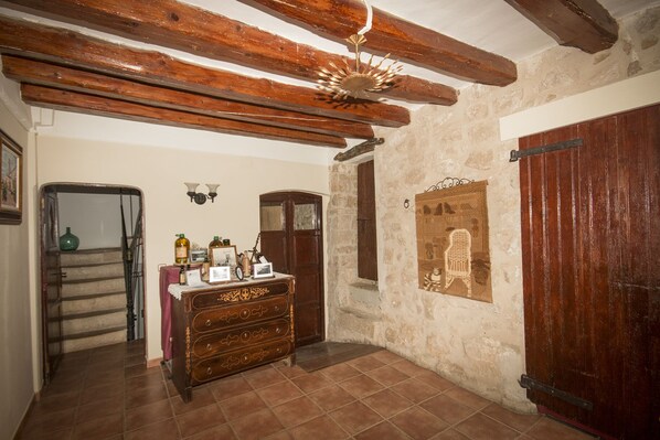 A rustic room with exposed wooden beams, a stone wall, a wooden chest of drawers, and a large wooden door.