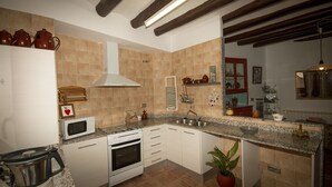 Une cuisine avec des meubles blancs, une cuisinière, un four à micro-ondes, un évier et une plante en pot.