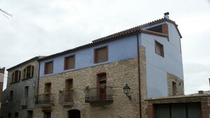Un bâtiment à deux étages, avec des murs en pierre et en crépi, un toit en tuiles et un petit balcon doté d’une balustrade en fer forgé.