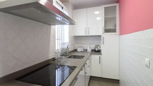 A compact kitchen with a black induction cooktop, white cabinets, a stainless steel range hood, and a window providing natural light. - Among magnolias, in the heart of the city ... (Córdoba)