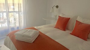 A hotel room with a neatly made bed, white bedding, and orange pillows. - Among magnolias, in the heart of the city ... (Córdoba)