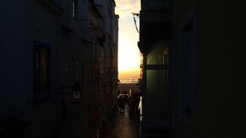 Un vicolo stretto fiancheggiato da edifici che conduce a una spiaggia al tramonto.