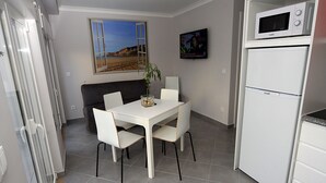 A compact kitchen with a white refrigerator, a microwave, and a dining area with a table and chairs.