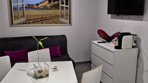 A modern living room with a white sofa, a dining table, and a TV mounted on the wall.