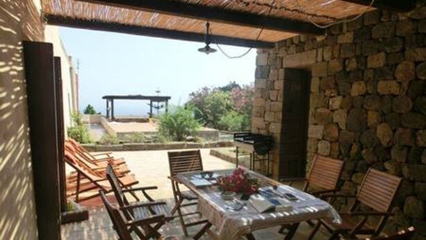 An outdoor patio with a table and chairs, a stone wall, and a view of the sea. - Dammuso number one (Pantelleria) (pantelleria)