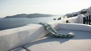 A white-walled room with a view of the sea and a distant island.