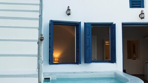 A white building with a small outdoor hot tub, two windows with blue shutters, and a wall-mounted light fixture.
