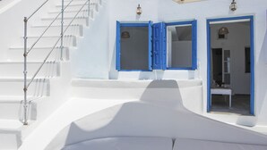 A white building with blue doors and windows, a staircase, and a small table with a chair outside.