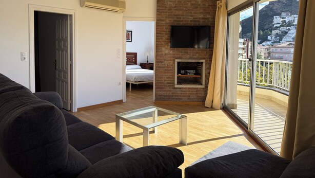 A living room with a sofa, a glass coffee table, a fireplace, and a TV mounted on a brick wall. - Agi Peater 3A Apartamento for rent in Roses Girona. (Roses)