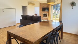 A modern dining area with a wooden table and chairs, a sofa, and a TV mounted on a brick wall. - Agi Peater 3A Apartamento for rent in Roses Girona. (Roses)