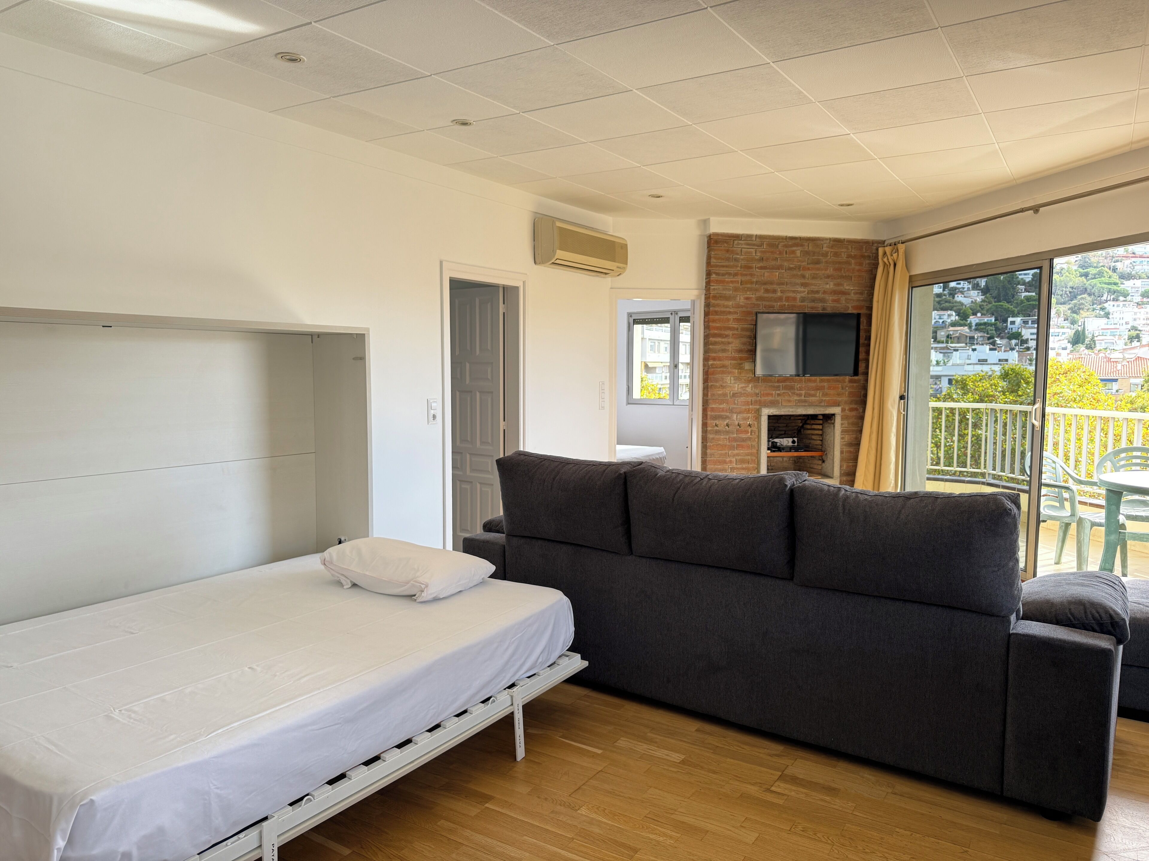 Une chambre moderne équipée d’un lit, d’un canapé, d’un téléviseur fixé au mur en briques et d’un balcon avec vue.