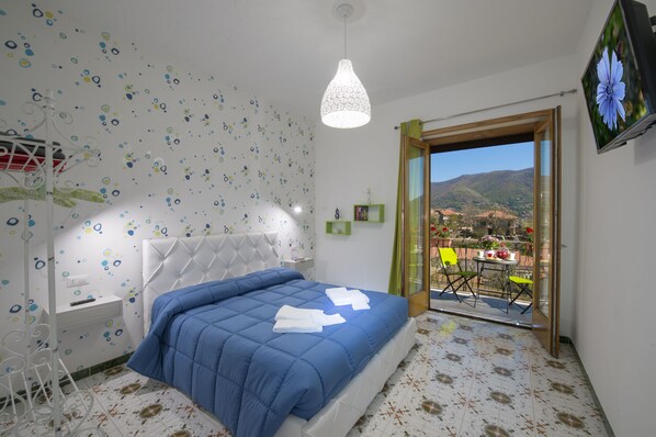 Une chambre à coucher avec un lit, une lampe suspendue, une vue à travers une porte vitrée et une petite table avec des chaises.
