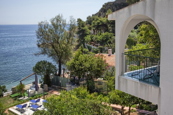 A seaside property with a balcony overlooking the sea, a garden with various plants, and outdoor seating.