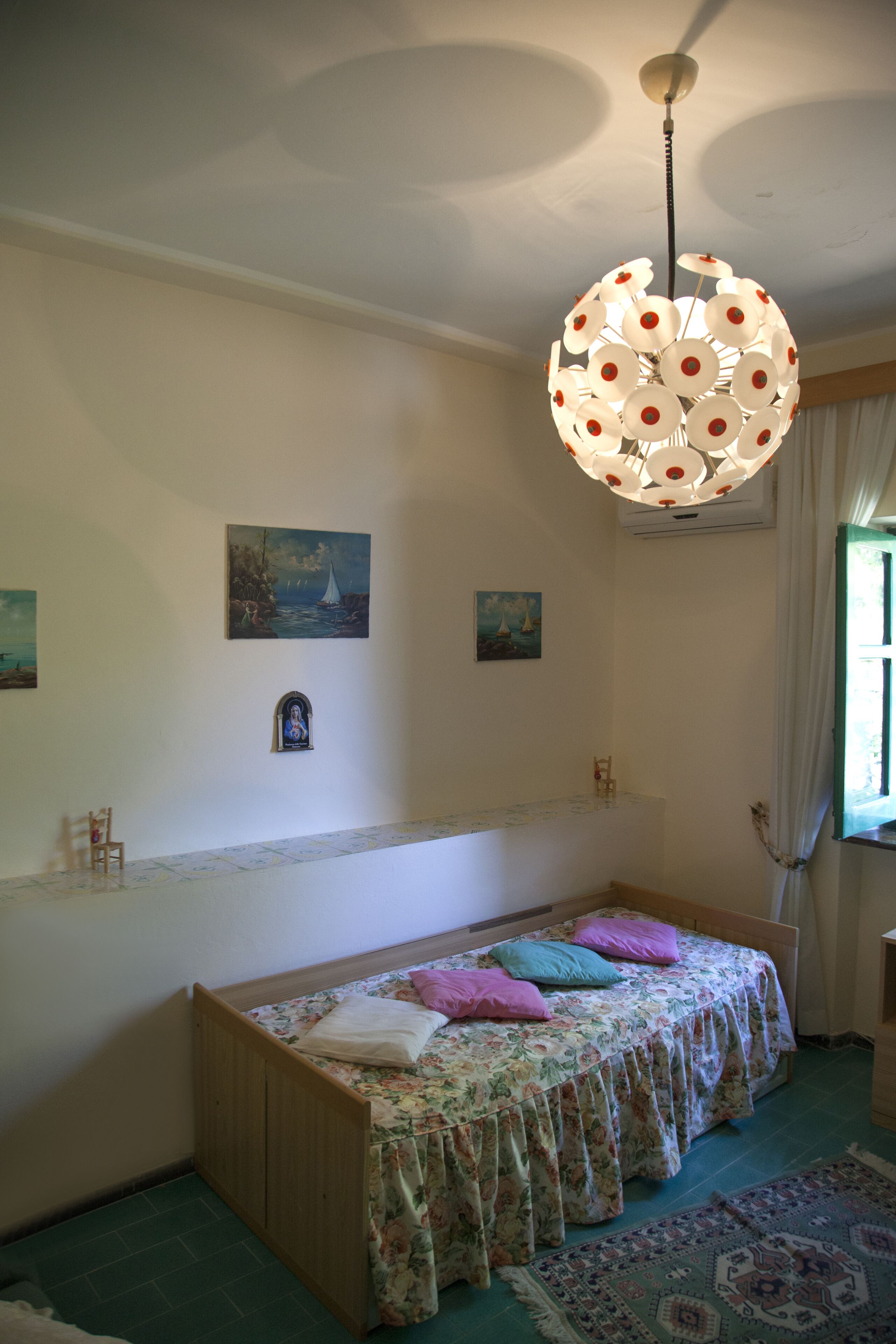 Une chambre avec un lit en bois, une couvre-lit à motifs floraux, un luminaire suspendu et des œuvres d’art murales.
