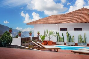 Ein Poolbereich mit Liegestühlen, Blumentöpfen und Blick auf Berge.
