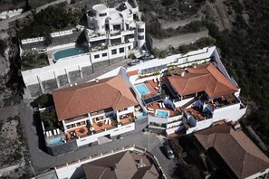 Ein Luftbild eines modernen Resorts mit mehreren Gebäuden, darunter ein großer Poolbereich und ein separates Gebäude mit rotem Ziegeldach.