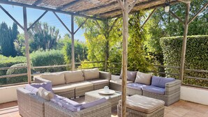 Een overdekt terras met rieten meubels en een pergola.
