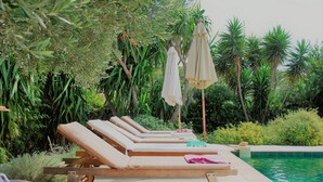 Een zwembadterras met ligbedden en parasols, omgeven door weelderige begroeiing.